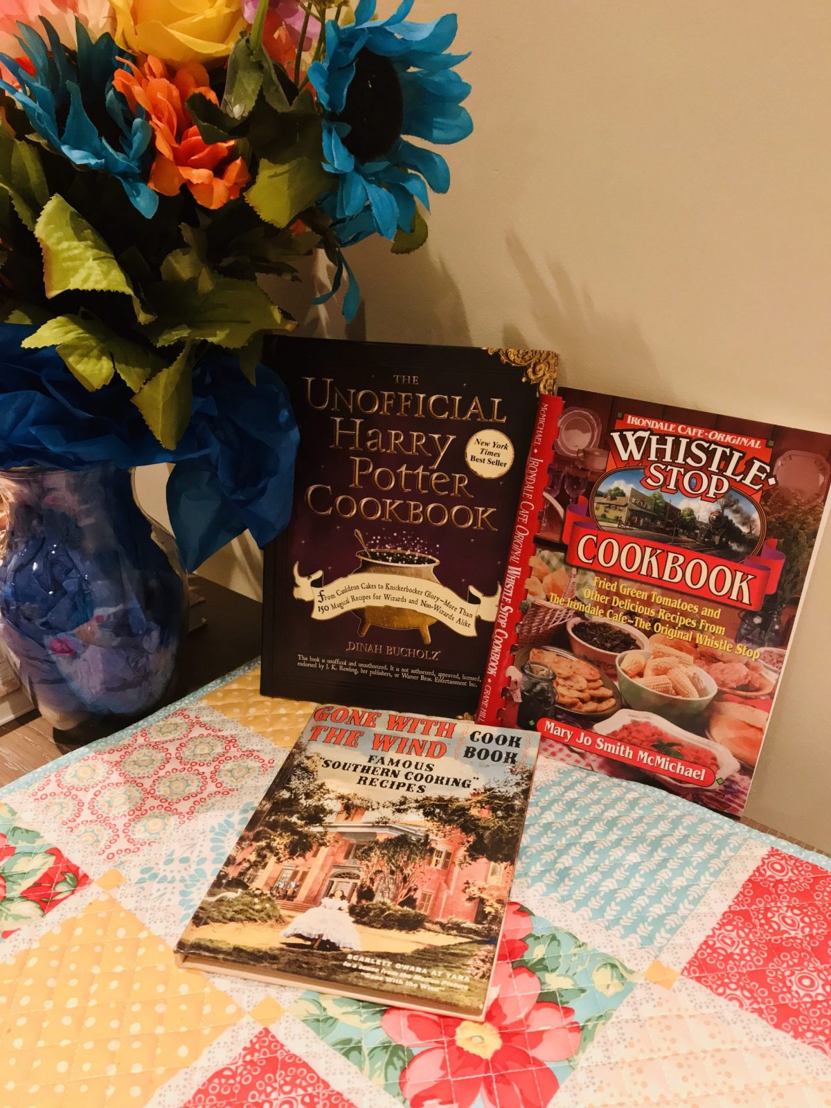 Photos of 3 of my themed cookbooks, against a backdrop of colorful place-mats and flowers.